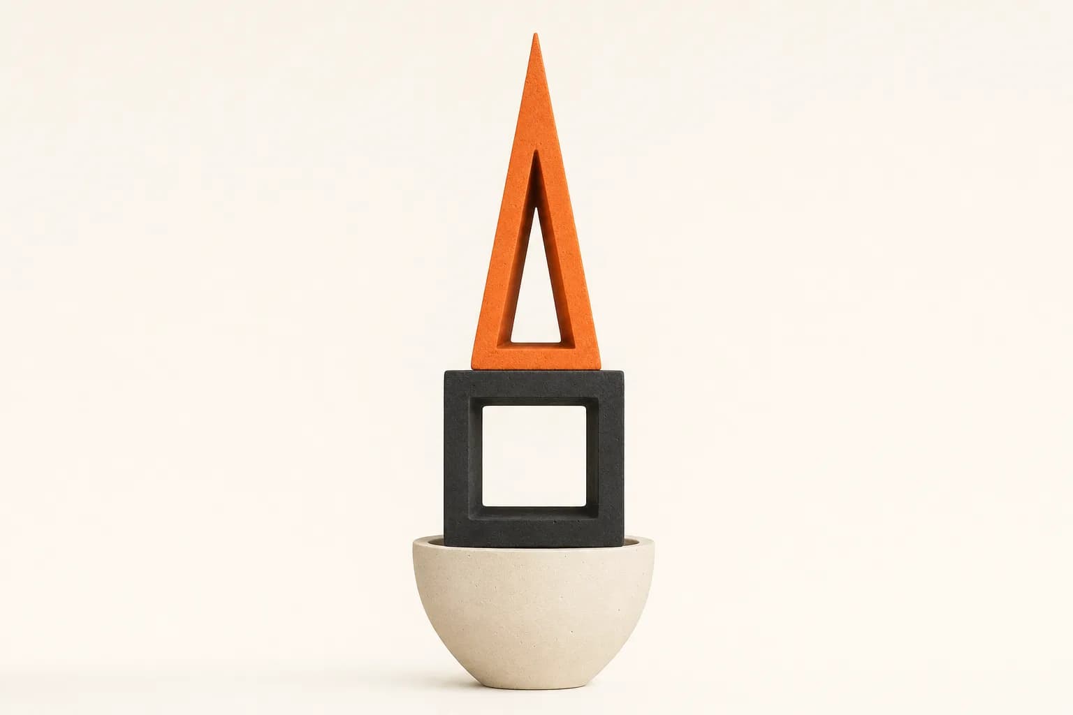 Matte ceramic totem photographed straight on: a tangerine open triangle crowning a black open cube, seated in an ivory bowl