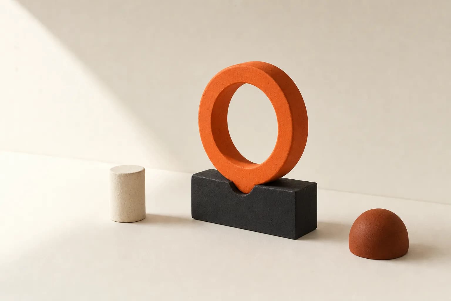 Matte ceramic still life: an upright tangerine ring held in a notched black block, an ivory cylinder to one side and a terracotta hemisphere to the other